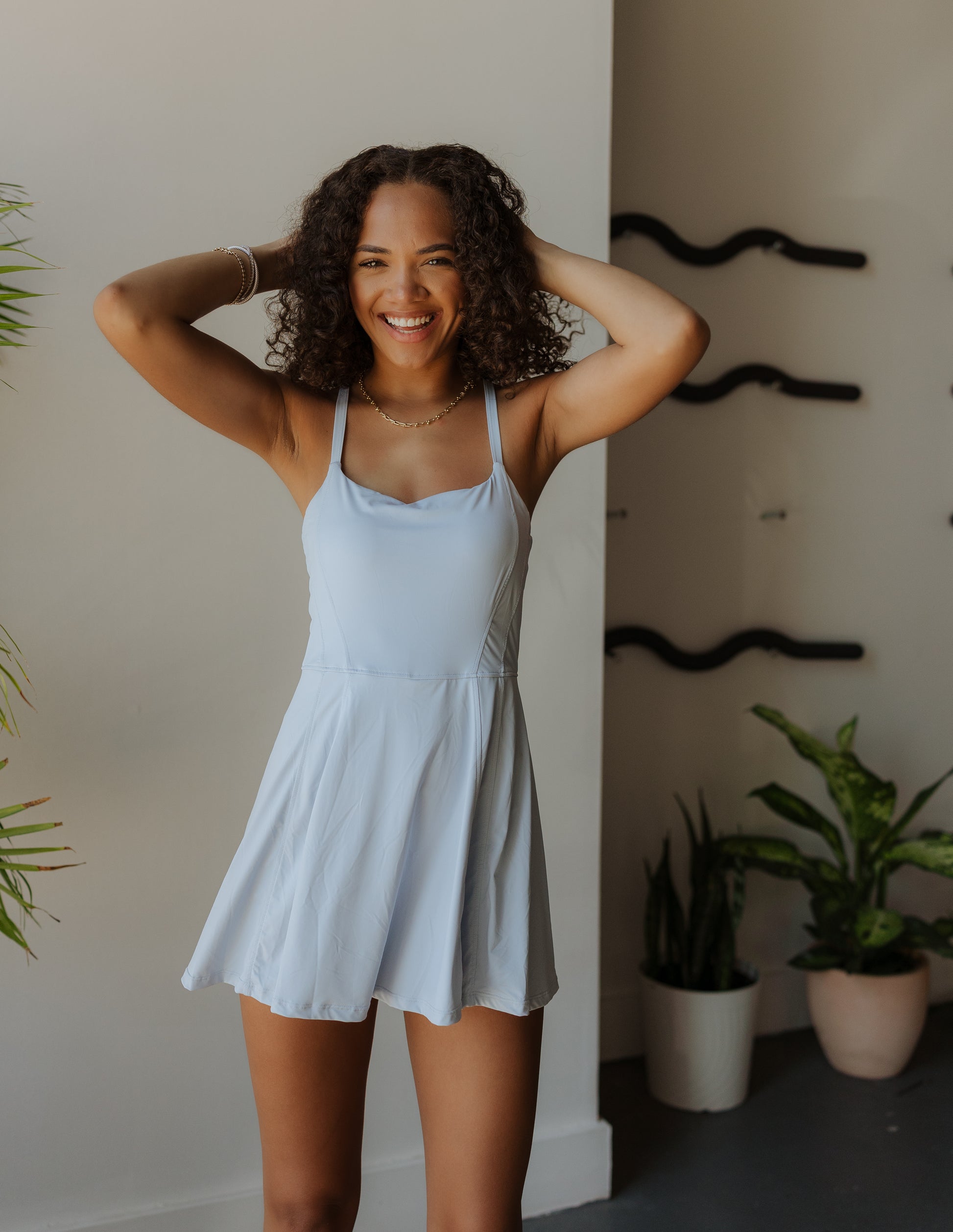 Woman in a light blue dress standing indoors with plants in the background