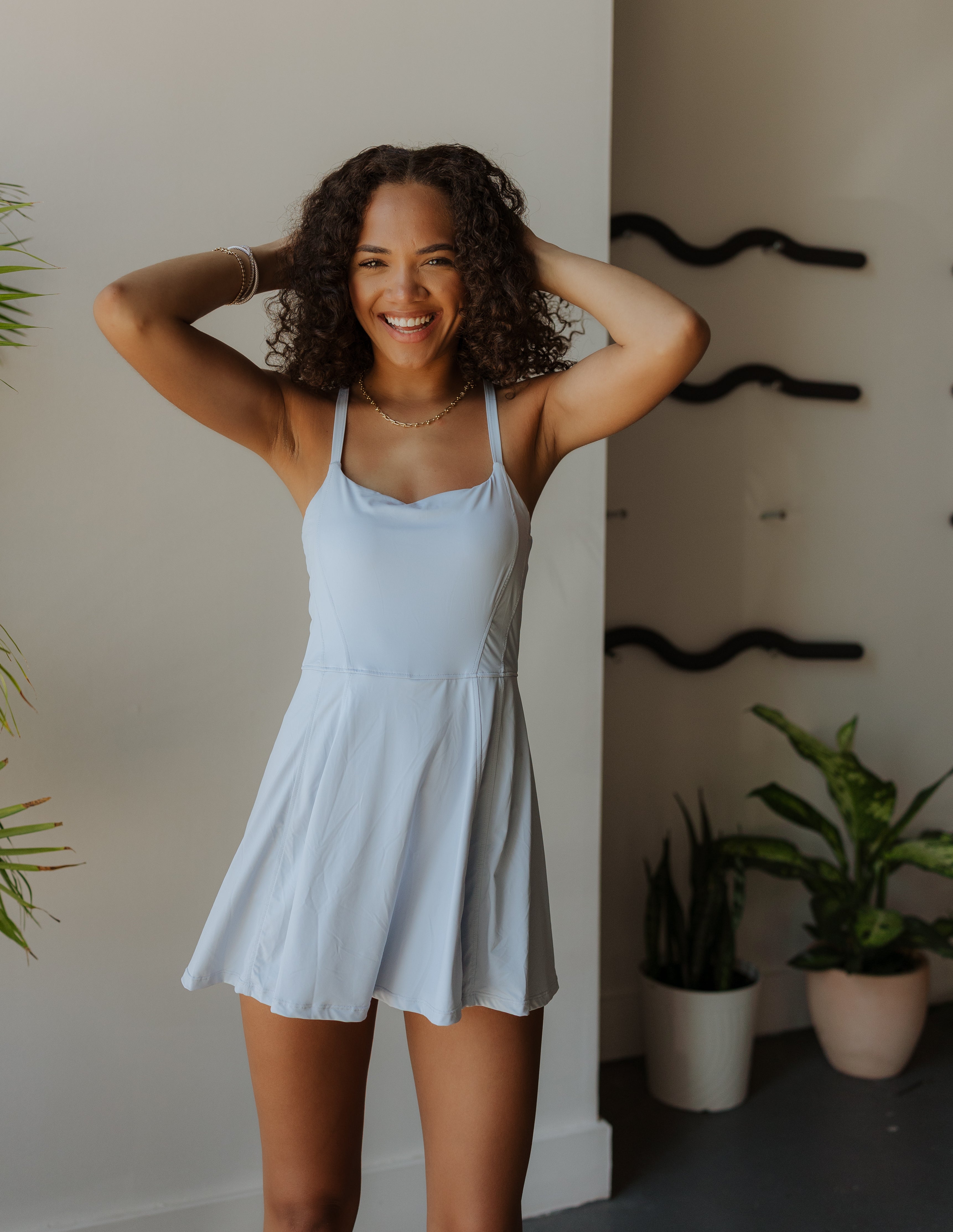 Woman in a light blue dress standing indoors with plants in the background