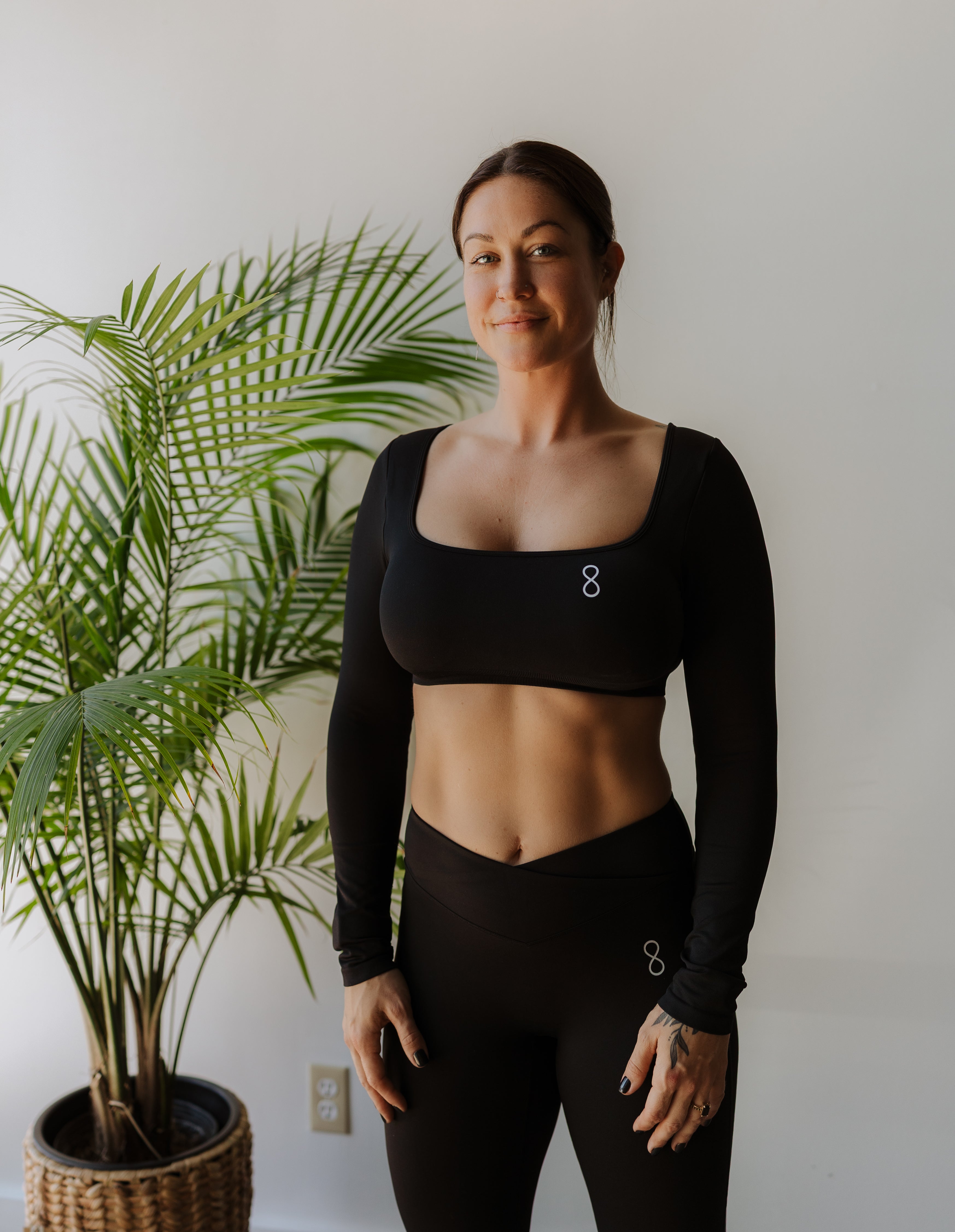 Woman wearing a black athletic outfit standing next to a potted plant indoors.