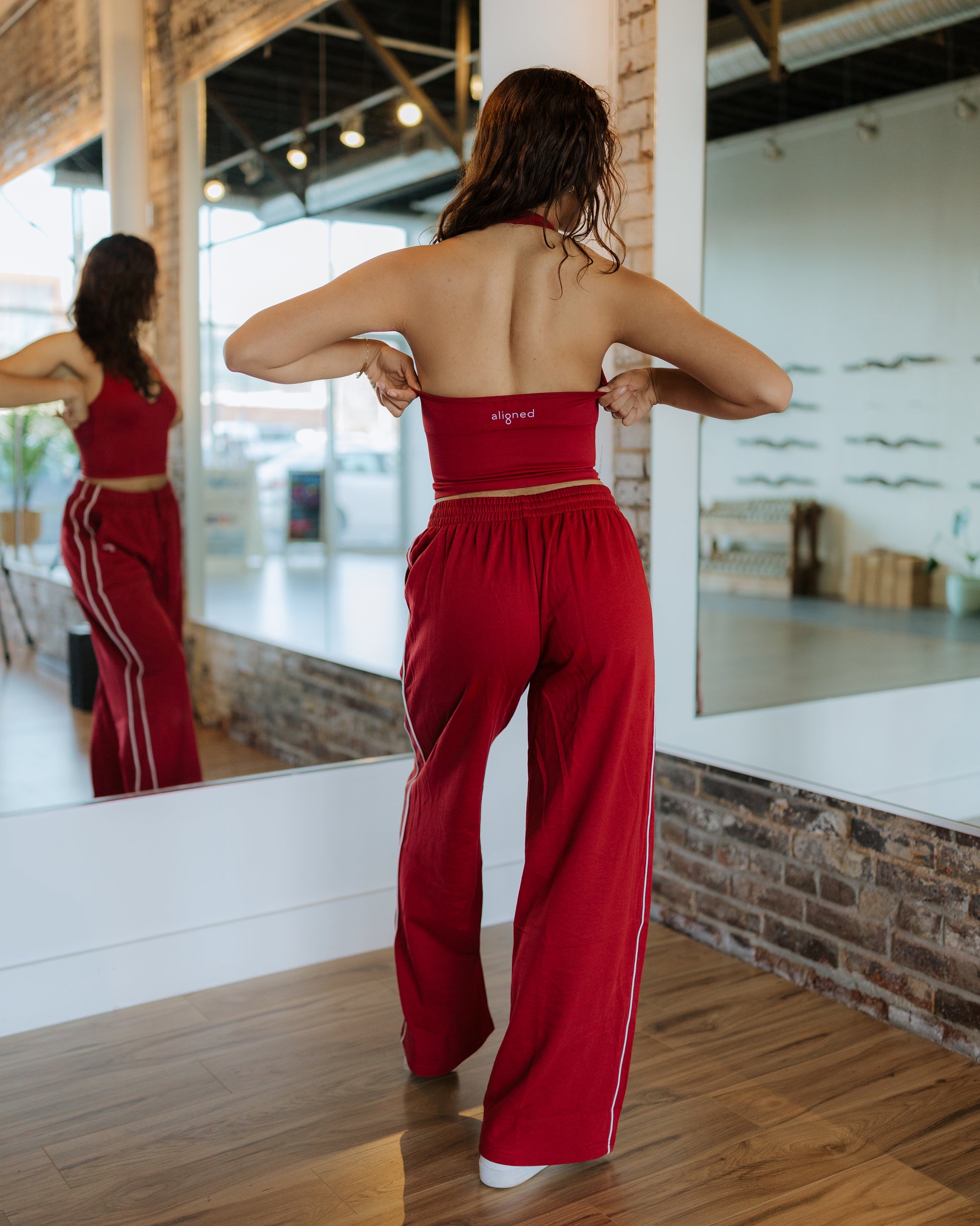 Woman in red outfit adjusting her top in front of a mirror.