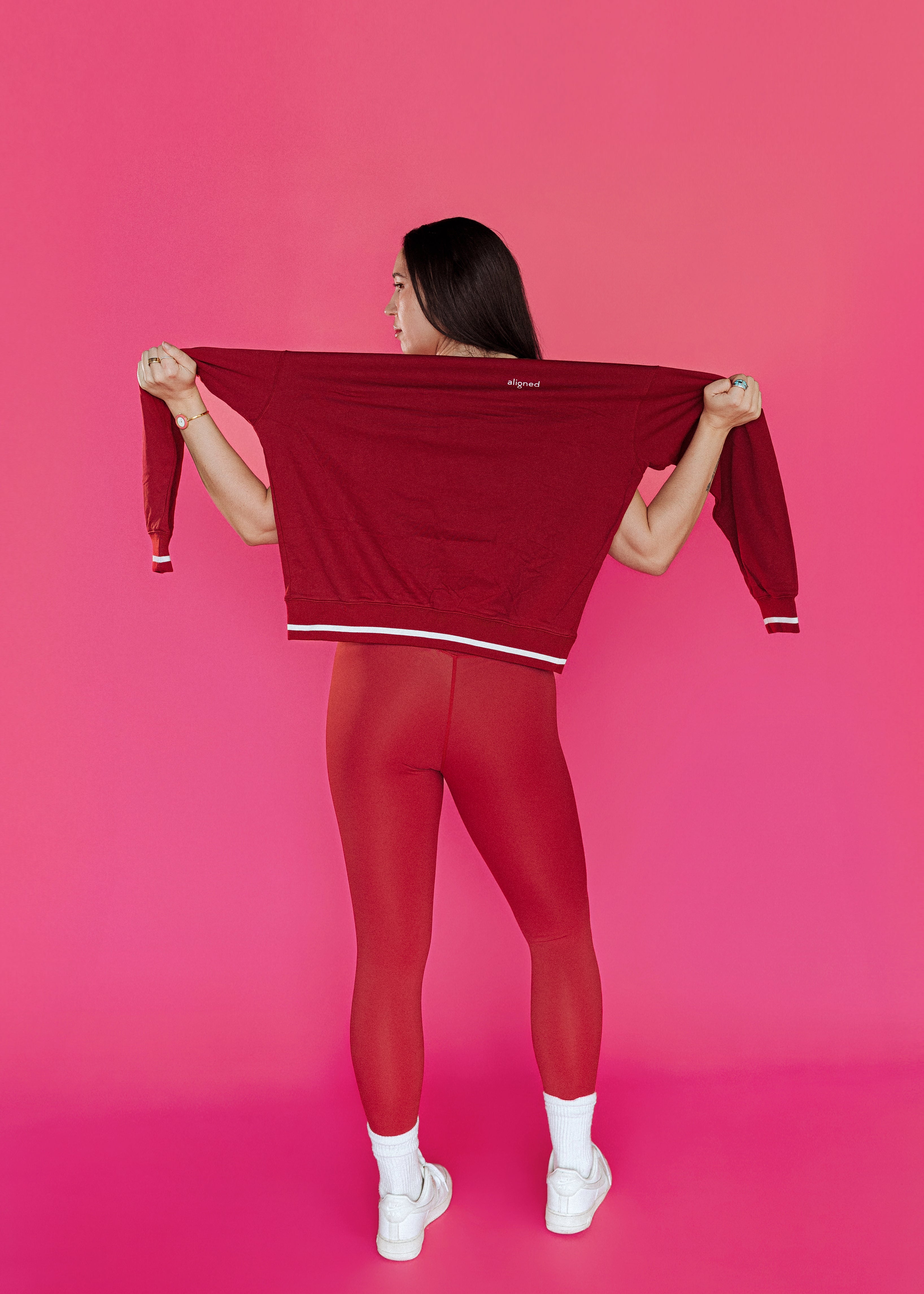 Woman wearing red workout set with red crewneck sweater standing in front of pink wall
