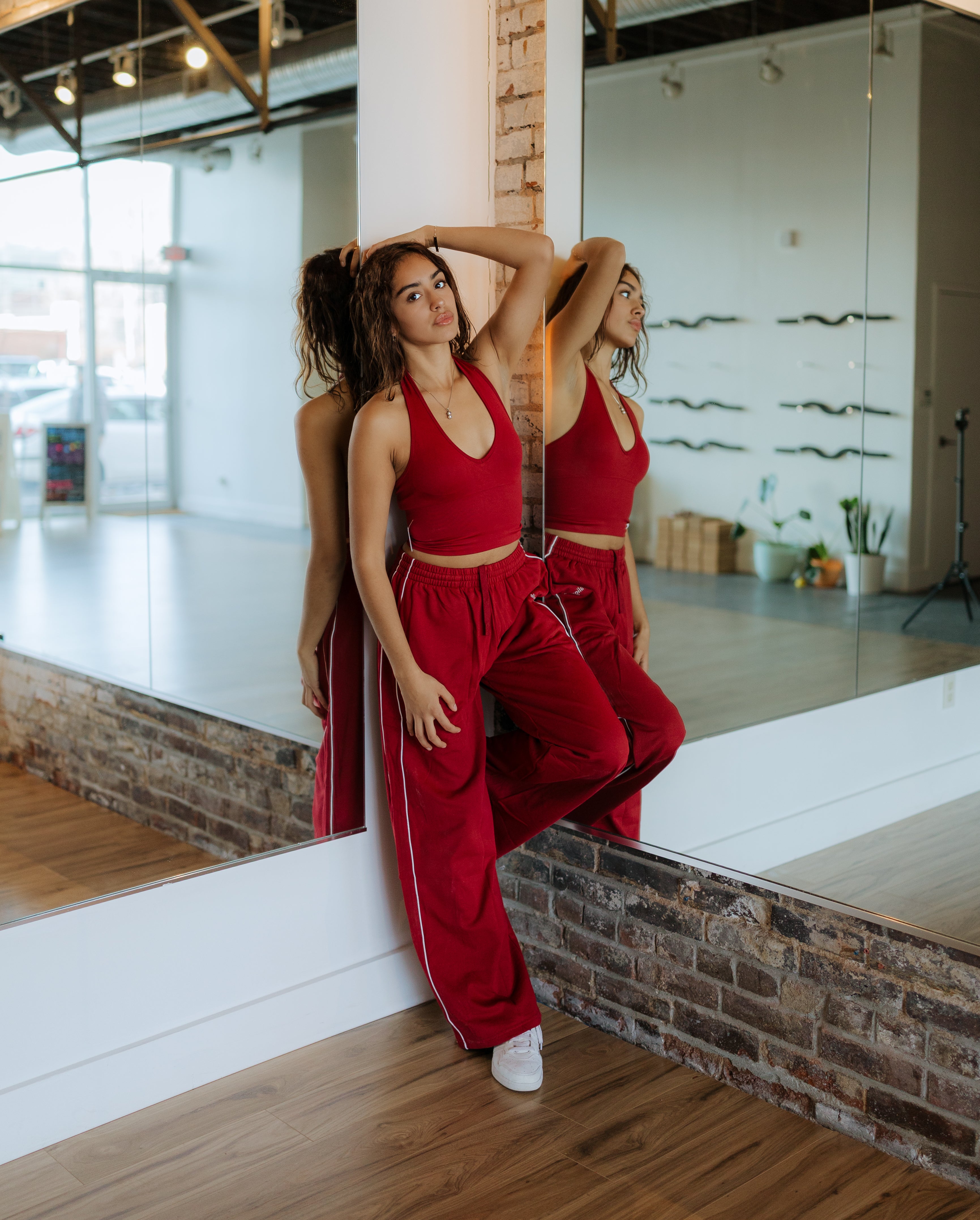 Woman in a red outfit posing in front of a mirror in a modern interior setting.